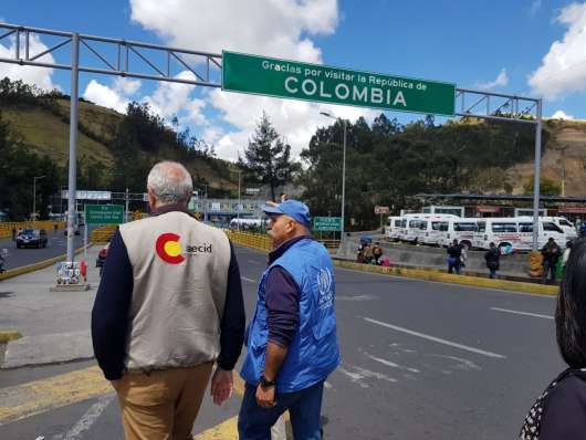 Dos hombre caminando con cartel de fondo en carretera